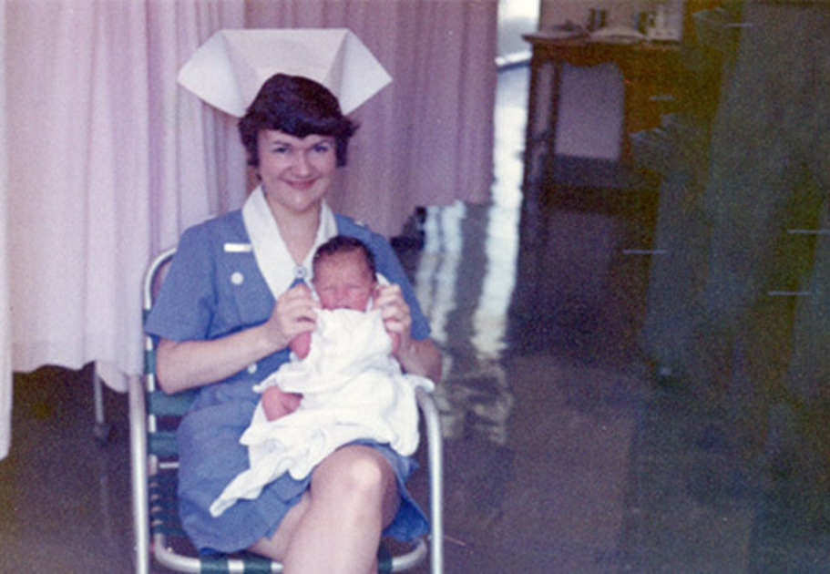 A young nurse, Lois, smiling as she holds a newborn in her lap — symbolising her lifelong care for others, continued through a gift in her Will to Mission Australia.