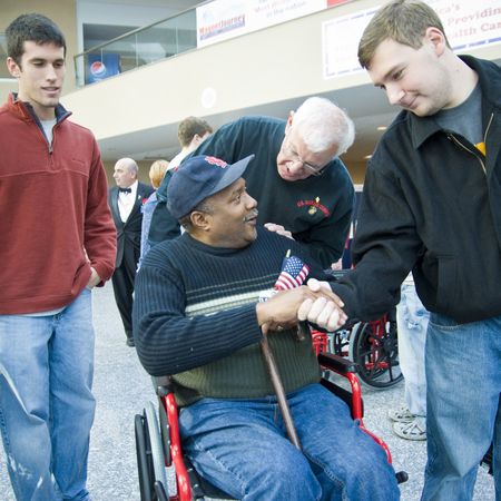 Col Chuck Gallina gives a wheelchair to a wounded vet with surrounding young Knights. 