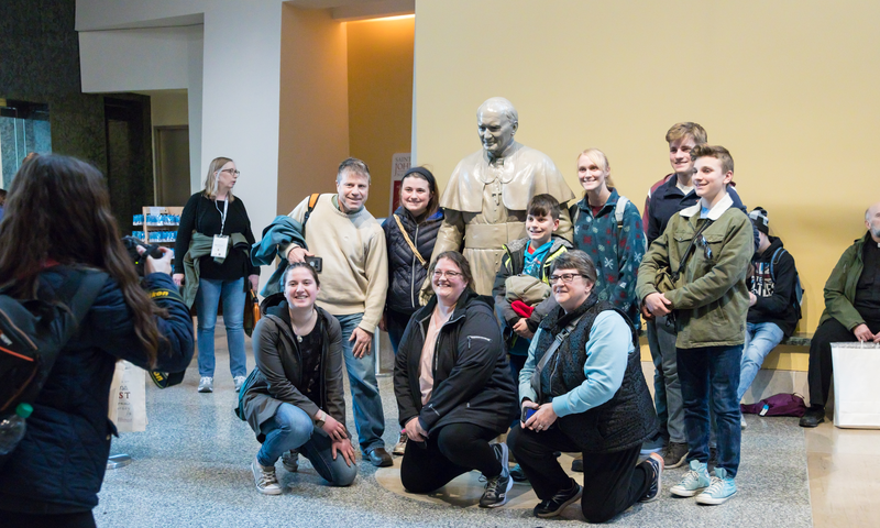 A group of pilgrims pose with a statue of Saint John Paul II on the lower level of the Shrine