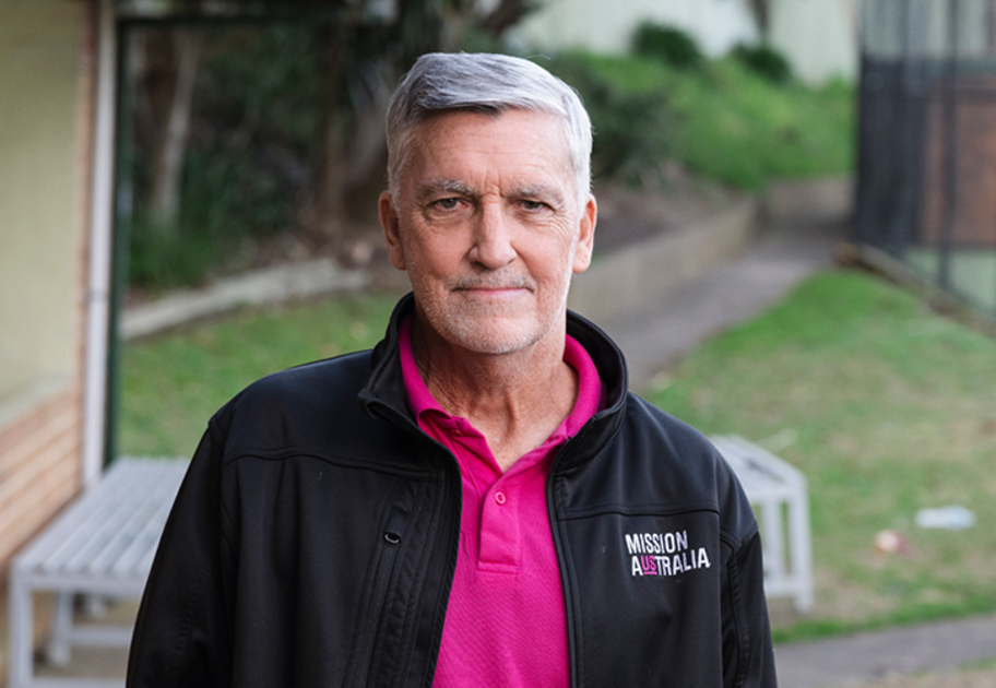 Mission Australia staff member standing outdoors wearing a branded black jacket and pink shirt.