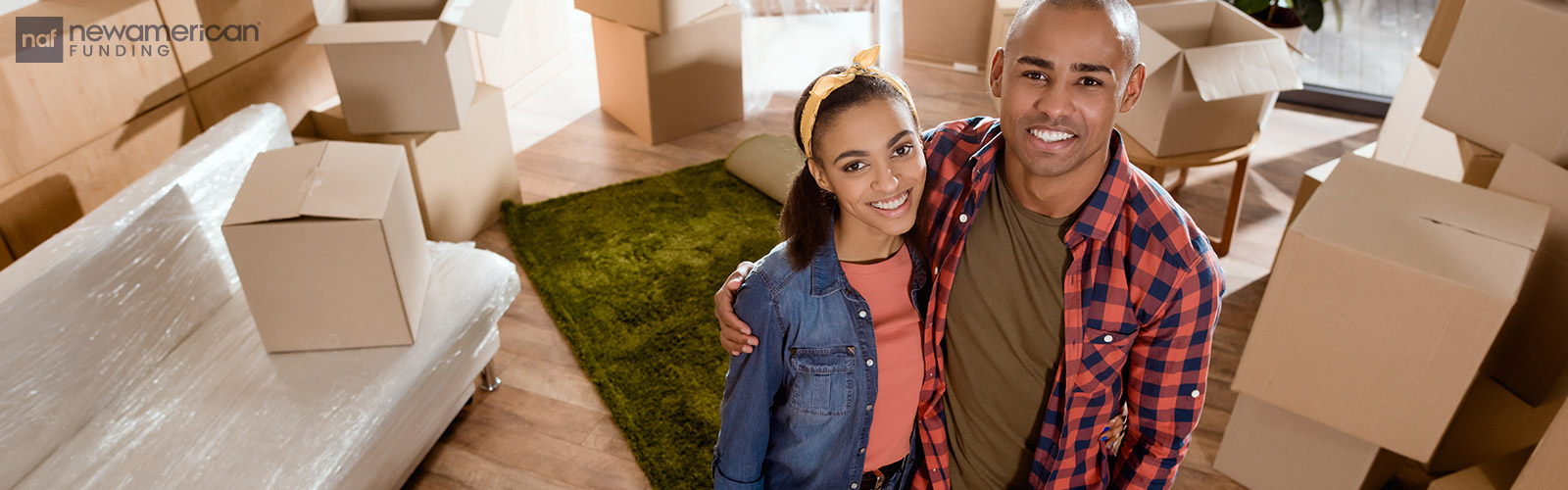 A happy Black couple smiles as they stand surrounded by moving boxes in their new home