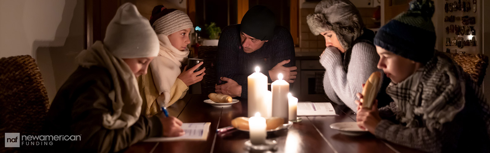 A man and woman and several kids sit bundled up around a table with candles in the center eating bread