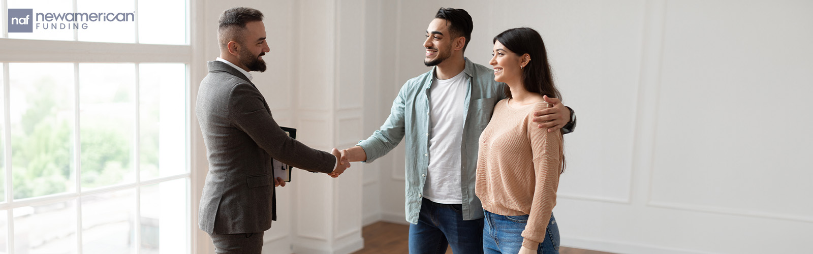 A housing professional shakes hands with a smiling couple inside their home