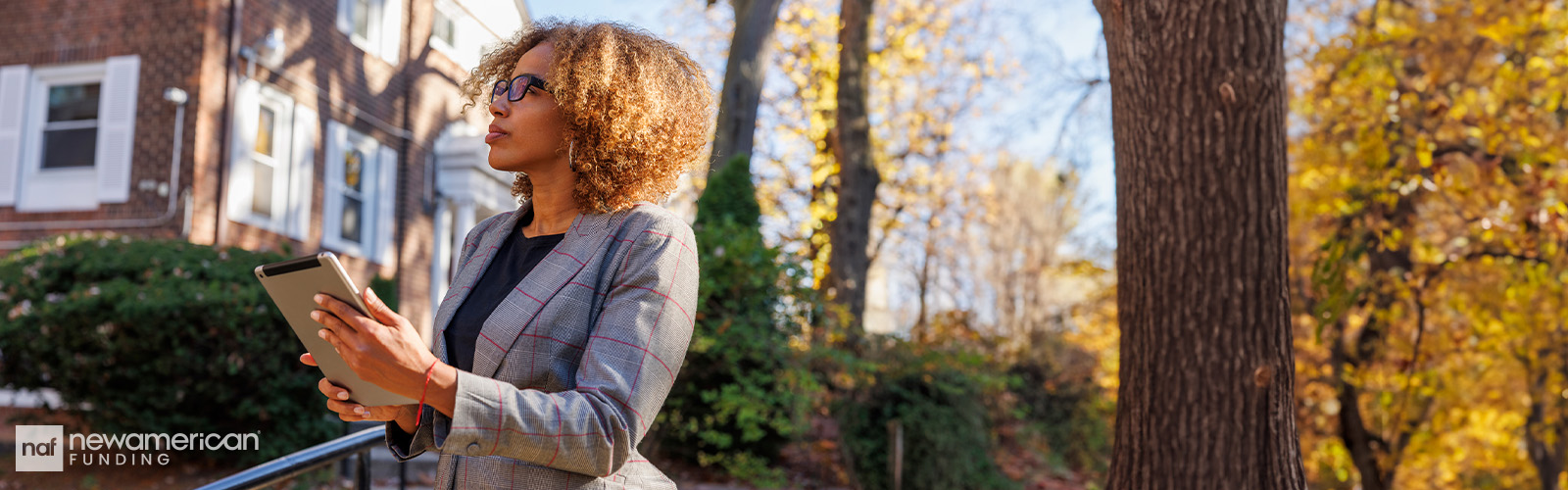 A Black woman stands holding a tablet and looking at a home