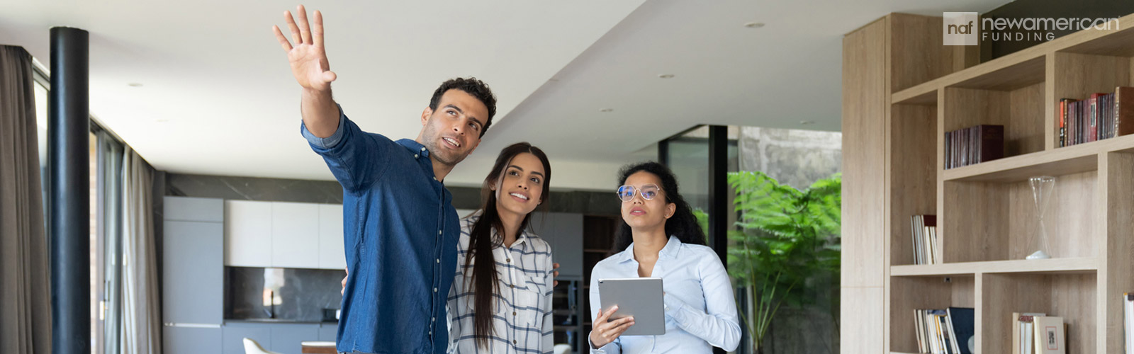 A man and woman stand smiling in a home while they talk to a woman holding a tablet