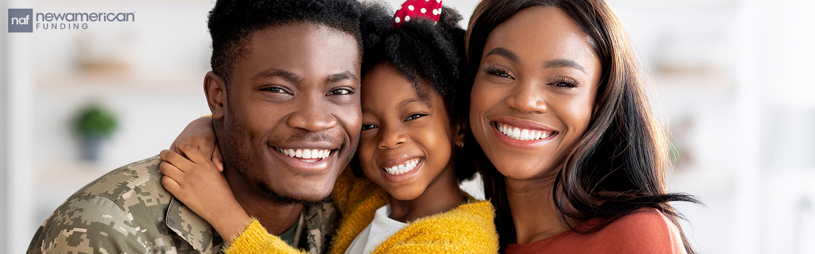 A Black man in a military uniform smiles into the camera next to a smiling Black woman and child 