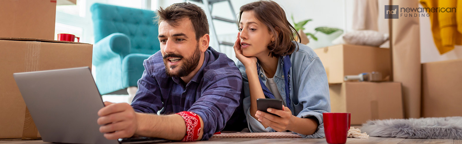 a couple lays on the floor in their living room looking at a tablet together and talking 