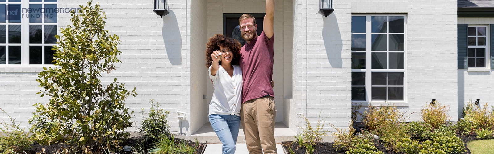 a Black woman and a white man stand together smiling and holding house keys in front of their new home