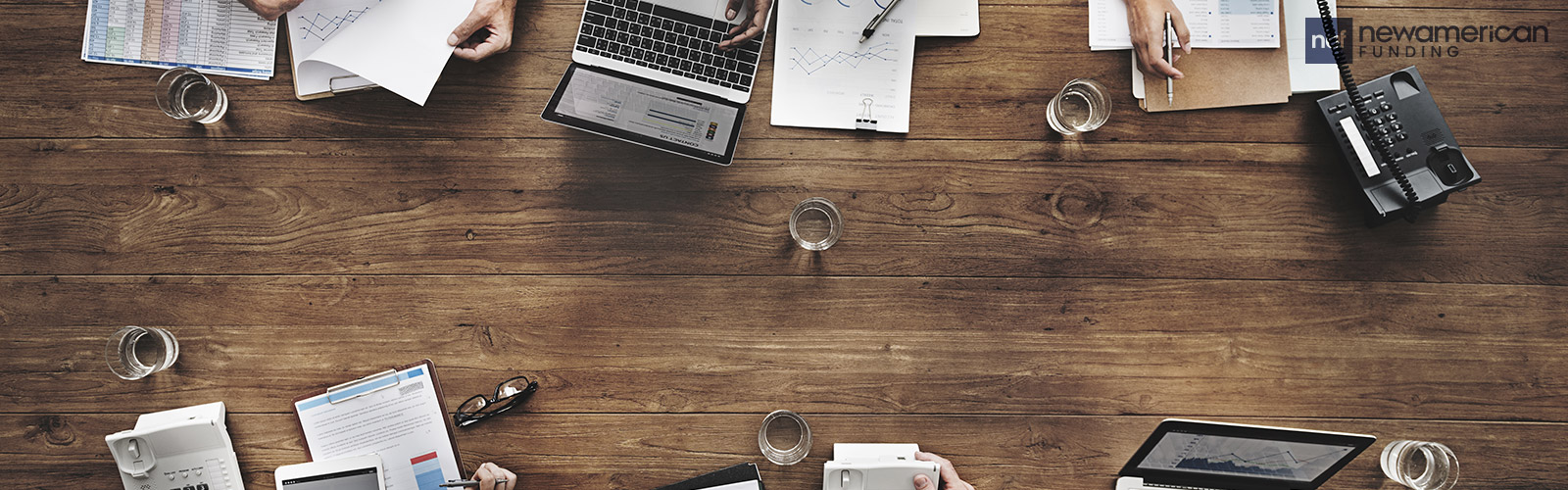 An overhead view of different work tools like laptops, a tablet, and papers sitting on a desk