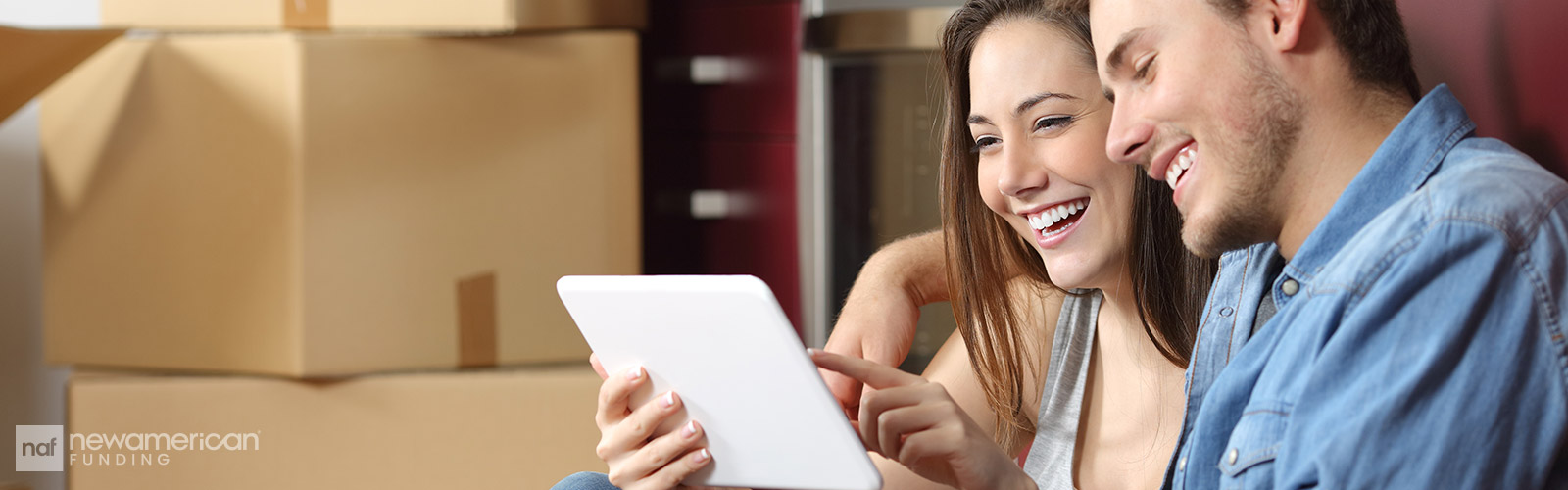 young, happy couple sitting on the kitchen floor on their tablet while  moving into their new home