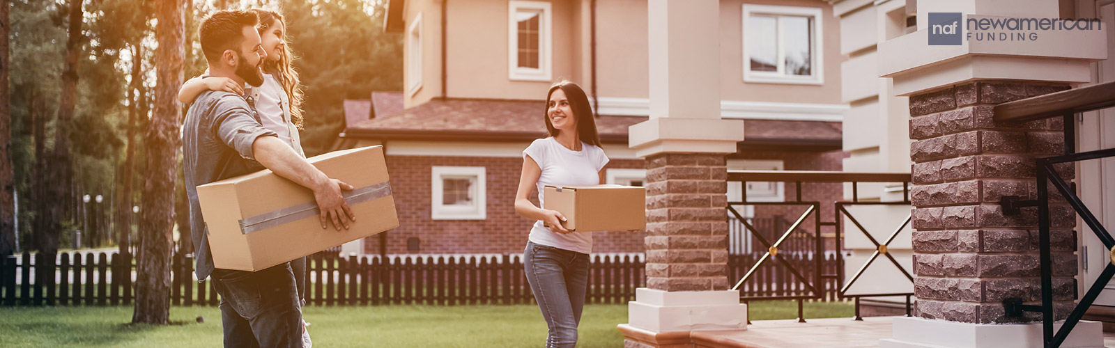 A smiling man and woman carry cardboard boxes into a home