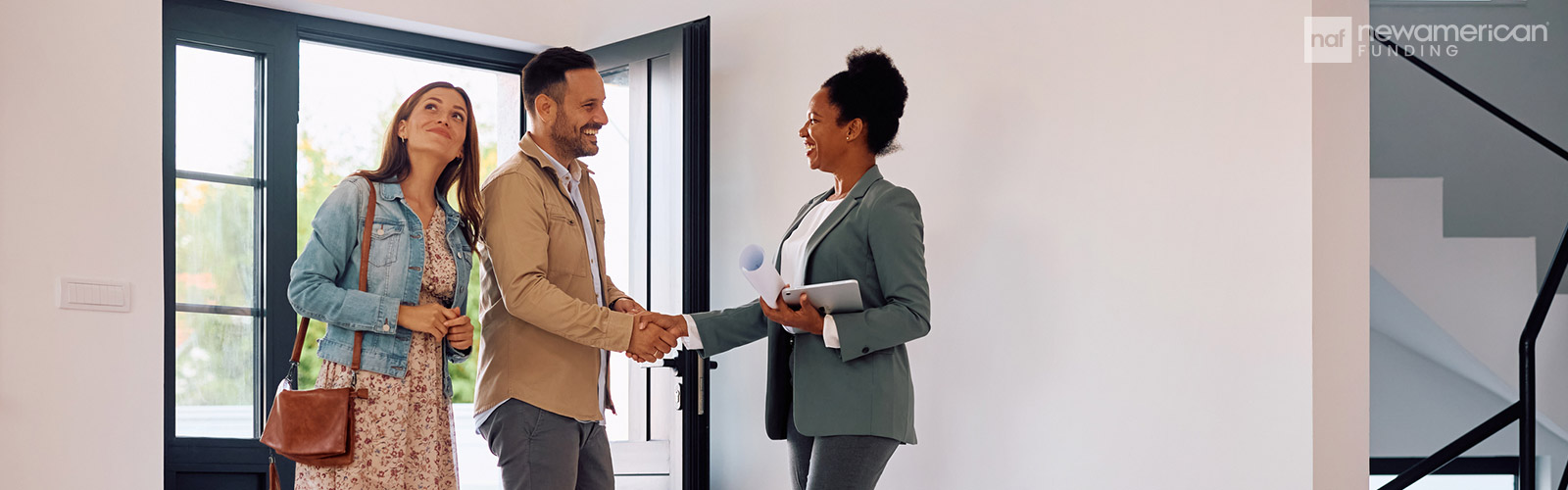 A Black woman in a suit shakes a white man's hand as he and another woman stand in the entryway of a home