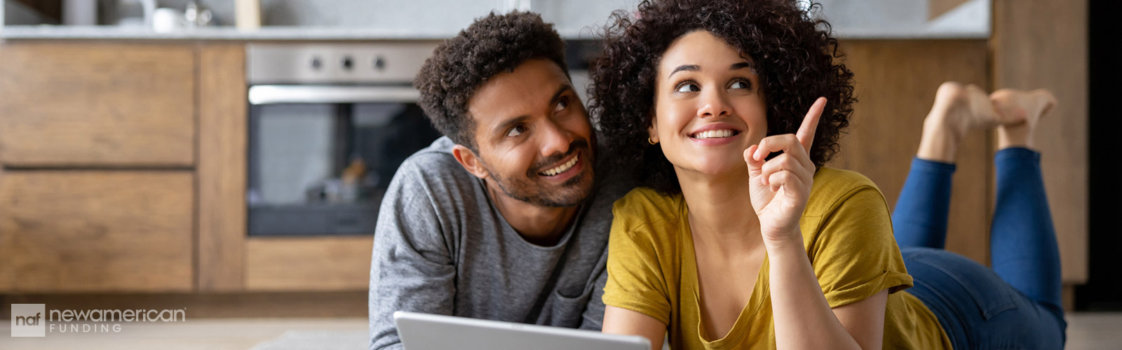 A Black woman and man sit smiling in their home as they plan their future