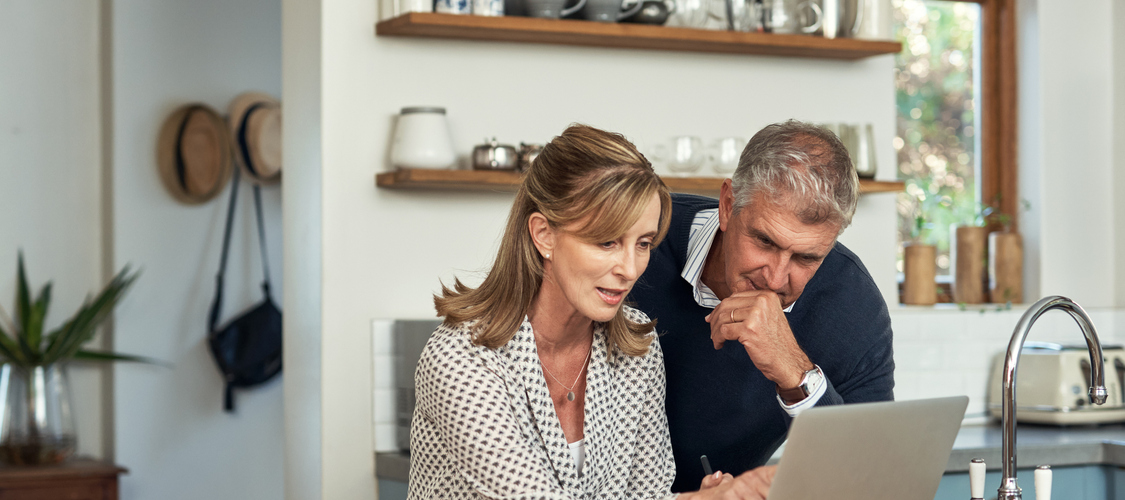 An older couple sitting at a table at home looking at laptop.