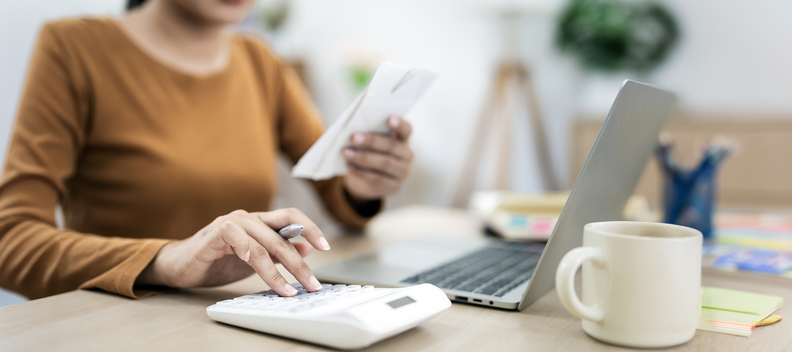 A woman in front of a laptop using a calculator.