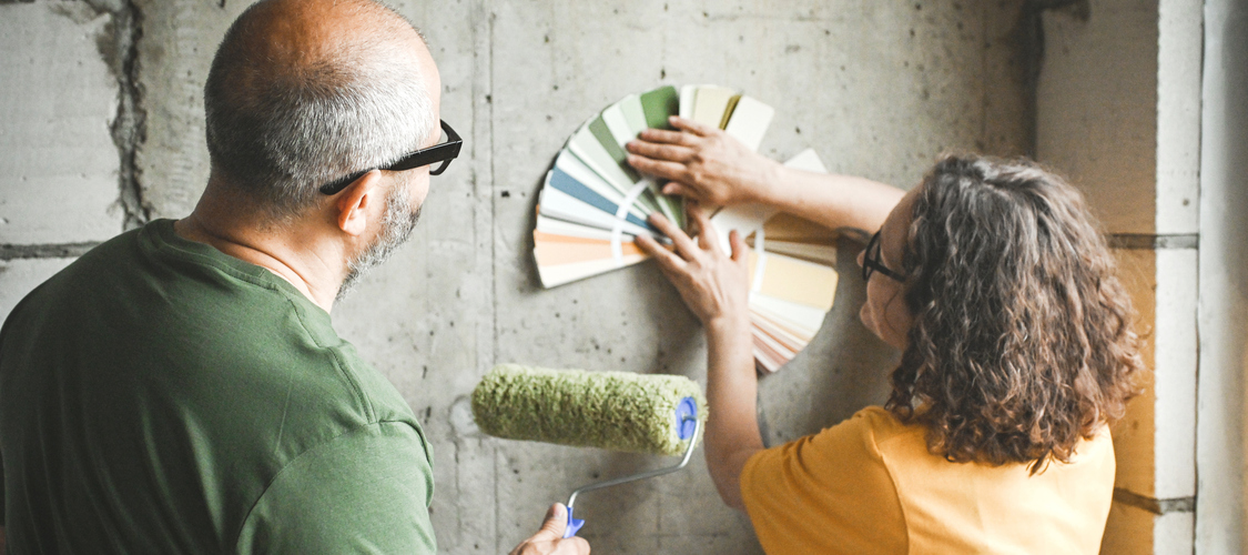 A middle-aged couple holding paint swatches up against a wall.