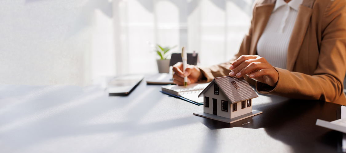 Someone sitting at a desk with paperwork and a block of a house.