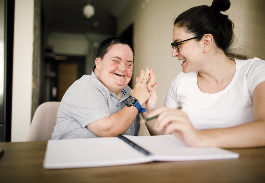 A man with Down syndrome giving a high five to a woman as they look through a workbook together.