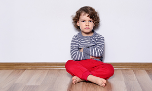 Kodrolas deček sedi na tleh s prekrižanimi nogami in prekrižanimi rokami kujavo zre v kamero.