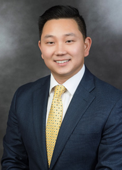 Headshot of Joseph Novak, who smiles while wearing a black suit and a yellow tie