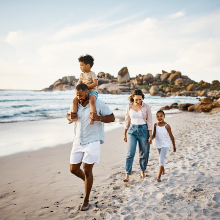 A family strolling on the beach, accompanied by their children, enjoying a leisurely walk by the shore.