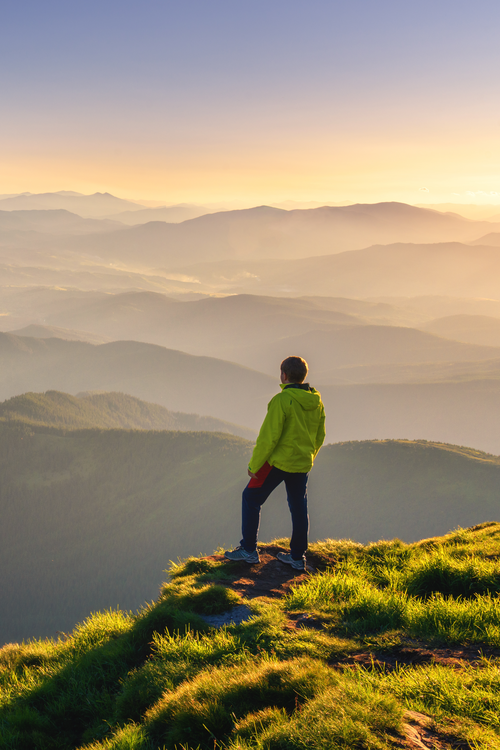 A man stands on a mountain peak, gazing at the vast valley below him