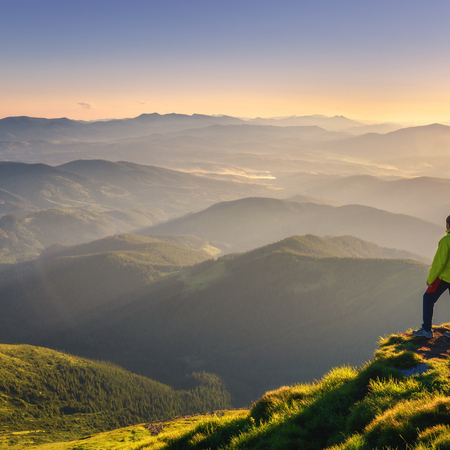 A man stands on a mountain peak, gazing at the vast valley below him