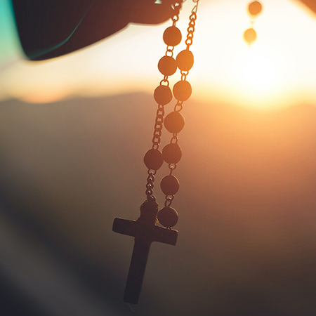 A rosary hanging from a car window at sunset, symbolizing faith and devotion.