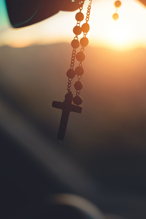 A rosary hanging from a car window at sunset, symbolizing faith and devotion.