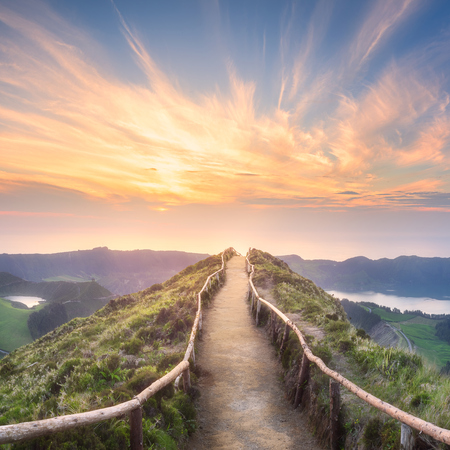 A scenic path ascends to the mountain peak as the sun sets, creating a breathtaking view.