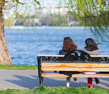 Simbolna slika za nasvet o možganski kapi in njenih posledicah - dve dekleti sedita na klopi ob jezeru na sončen spomladanski dan.