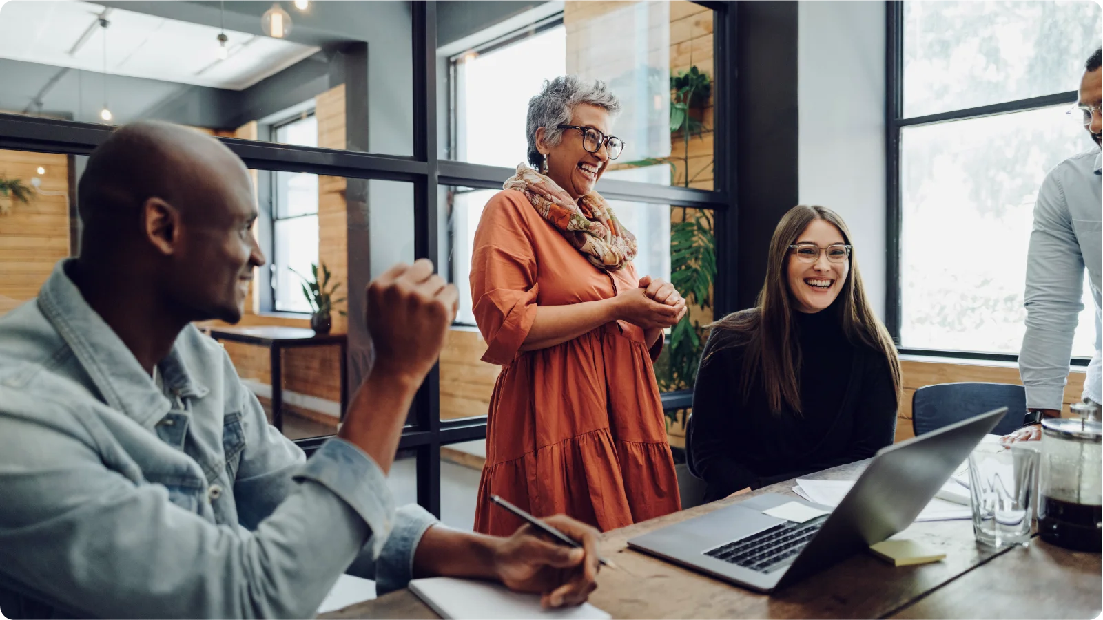 Three smiling, casually-dressed professionals surrounding a conference room in a modern office space