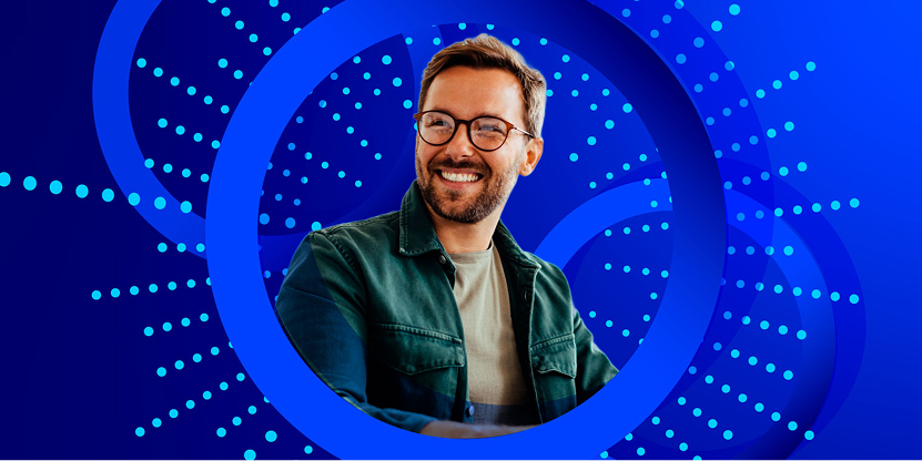 A smiling man with a beard and round glasses, wearing a dark green jacket over a light t-shirt, looks away and to the side. He is framed by large blue concentric circles and a vibrant blue background with radiating blue-dotted lines.