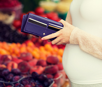 Nosečnica gleda v odprto denarnico. Simbolna slika za finančno varnost ob prihodu dojenčka.