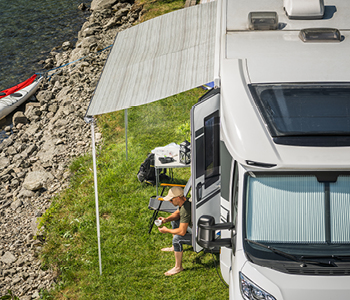 Avtodom, parkiran ob jezeru, kjer potniki lahko uživajo v hladu in miru.