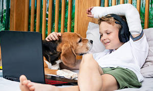 Deček s psom leži v postelji in gleda serije na računalniku. Roko ima v mavcu, ki je posledica padca - ene najpogostejših nevarnosti za otroke.