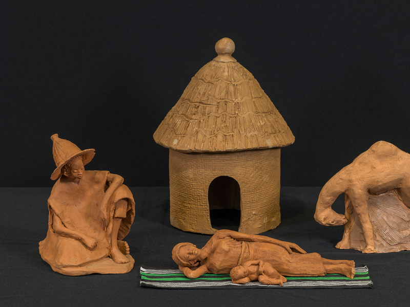 Crèche from Ghana by Mohammed Amin with the Holy Family, camel, hut, and woven carpet. Mary reclines with the Christ Child beside her.