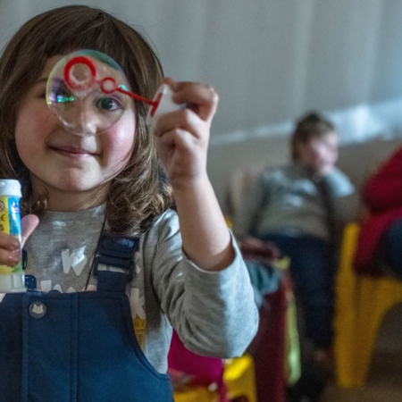 A young Ukrainian girl plays with bubbles in a refugee camp during war times.
