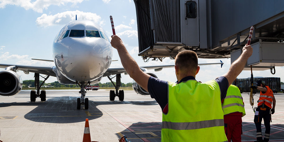 Person in hi-vis vest holding up signs, guiding a landing airplane