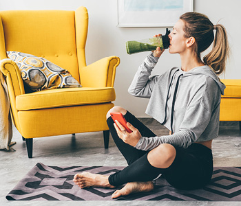 Mlada ženska začenja dan tako, da sedi na tleh in pije smoothie.