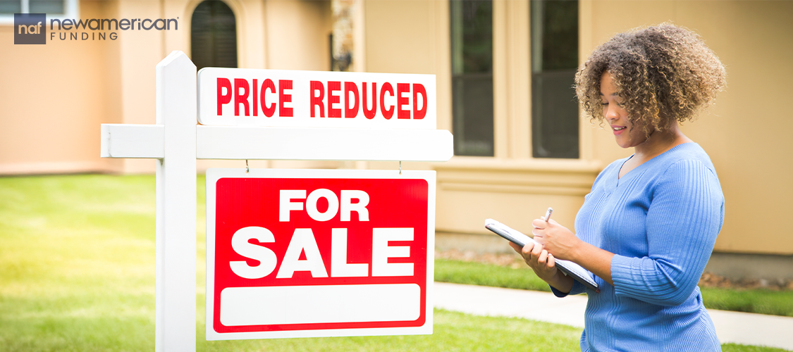 A woman looking at For Sale sign with a priced reduced sticker above it.