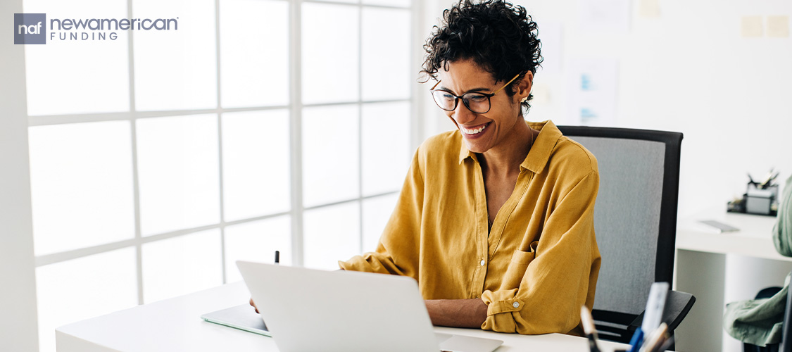 A woman smiling as she looks at a laptop.