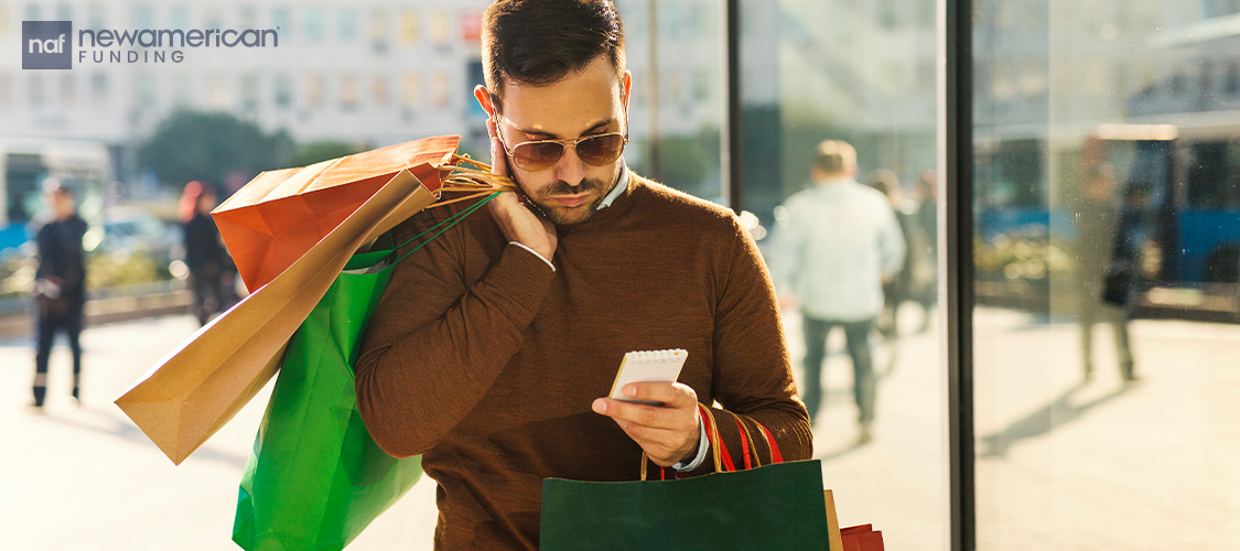 A man wearing sunglasses carrying a bunch of shopping bags.