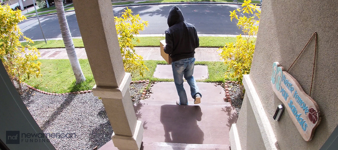 A man in a hoodie leaving a porch with a package.