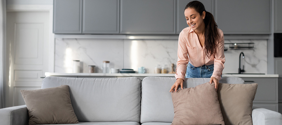 A woman fluffing pillows on a couch.
