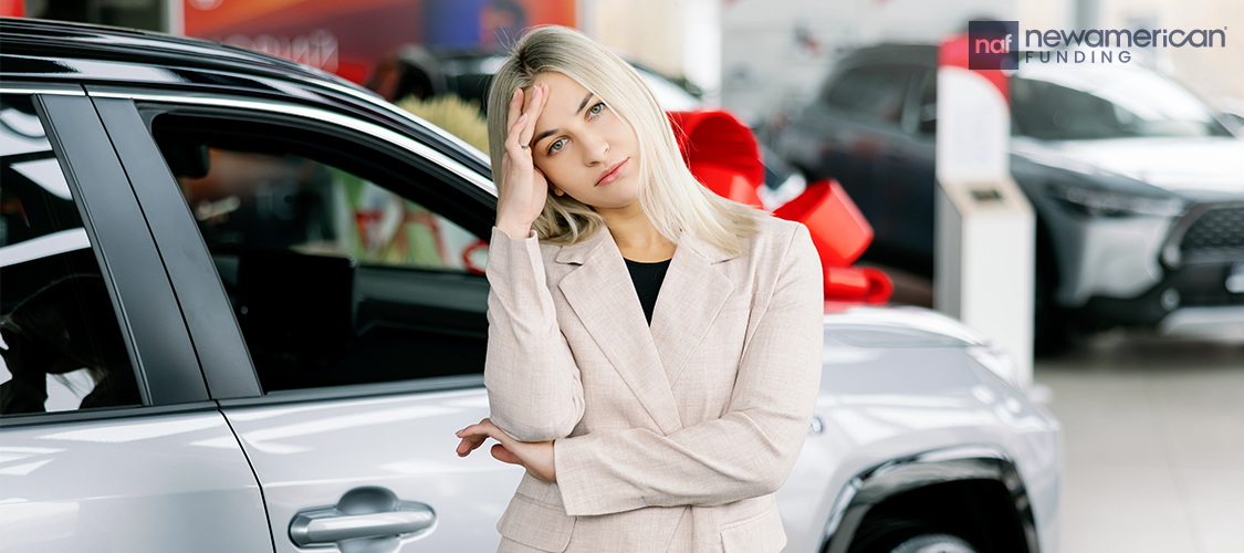 A woman who doesn't look happy standing beside a car with a bow on it.