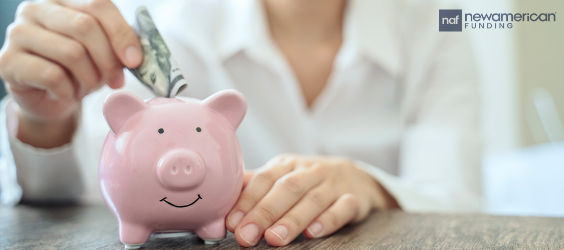 A hand putting a dollar into a piggy bank.