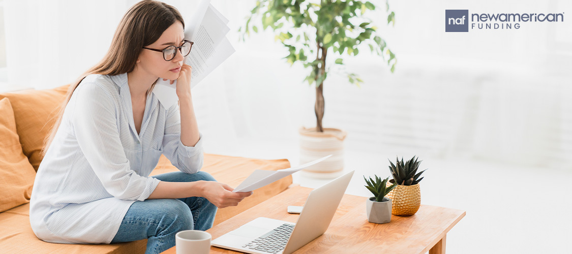 A woman sitting on a couch in front of an open laptop.