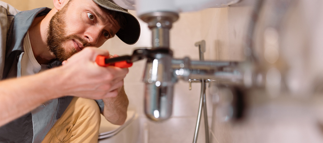 A man fixing a pipe underneath a sink.