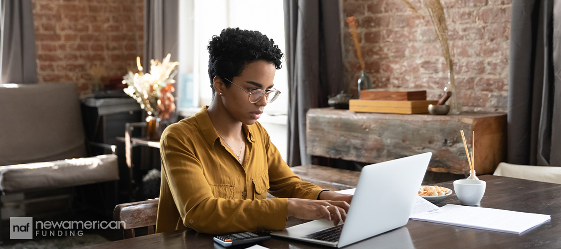 A woman sitting at a home desk on a laptop.